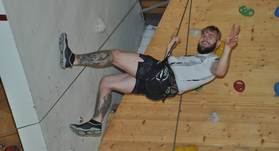 Ein Teilnehmer hängt an einer Indoor-Kletterwand. Er freut sich über seinen Erfolg. 